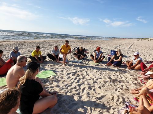 Nuotraukoje - stovyklos dalyviai susėdę ant smėlio pajūryje daro mankštą