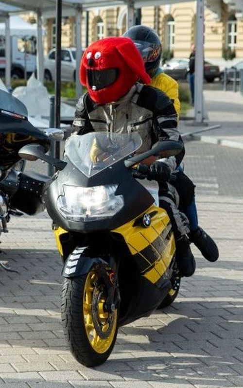 Nuotraukoje - motociklininkas, užsidėjęs ki&scaron;kio galvos pavidalo &scaron;almą su keleiviu
