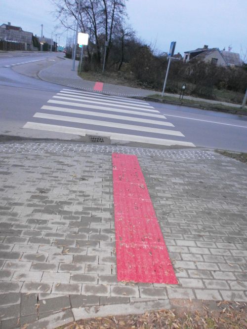 Nuotraukoje - T formos taktilinė danga padeda neregiui lengviau pereiti gatvę, o raudonas tako kontrastas padeda silpnaregiams lengviau orentuotis mieste