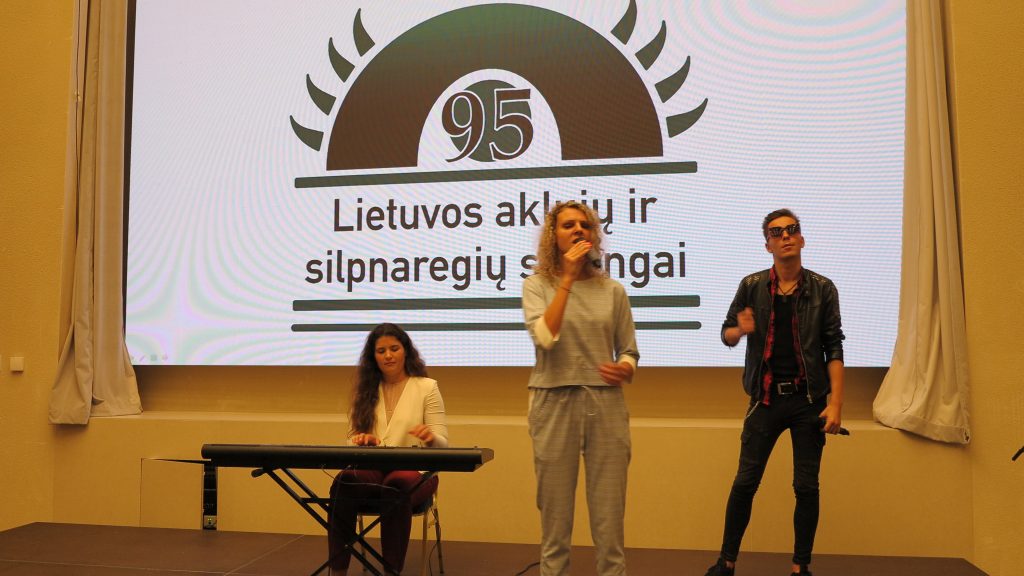 Nuotraukoje - G. Sidiniauskas ir "Vėjų rožės" atlikėjos scenoje, jiems už nugaros LASS 95-mečio emblema